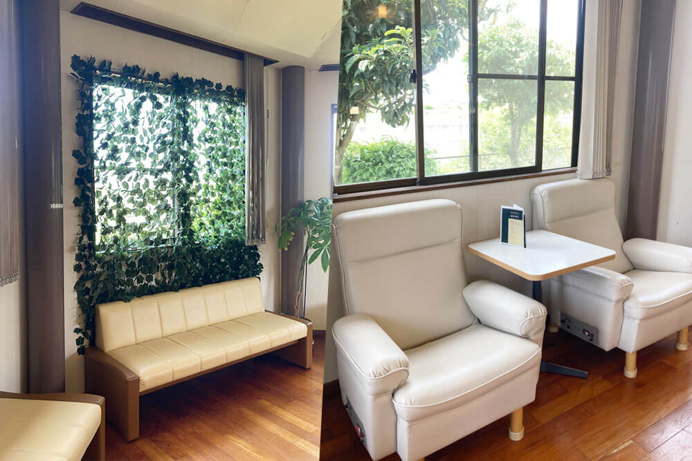 富士たちばなクリニック待合室 造花のグリーンカーテンのある窓の置かれているソファと明るい雰囲気のなかにあるオットマンのあるソファ